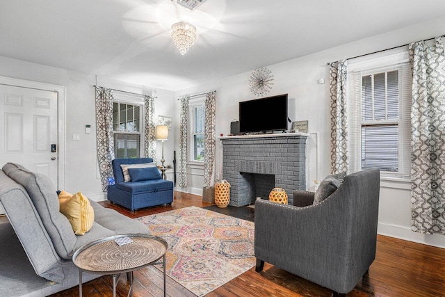 living room featuring a brick fireplace, an inviting chandelier, and dark hardwood / wood-style flooring