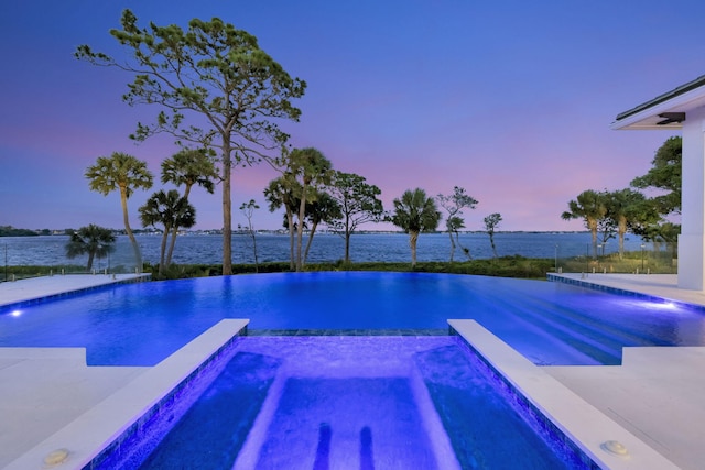 pool at dusk with an in ground hot tub and a water view