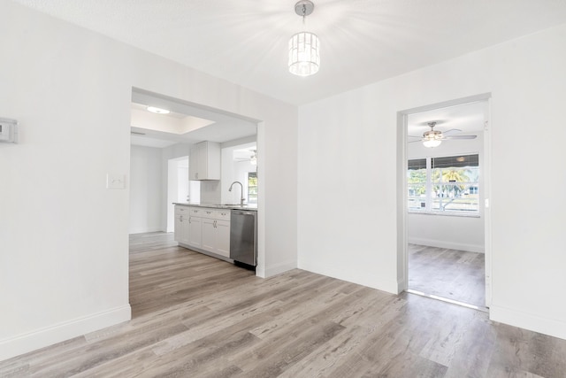 interior space featuring stainless steel dishwasher, sink, pendant lighting, light hardwood / wood-style flooring, and white cabinets