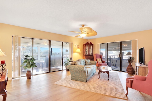 living room with ceiling fan, a textured ceiling, and light hardwood / wood-style flooring