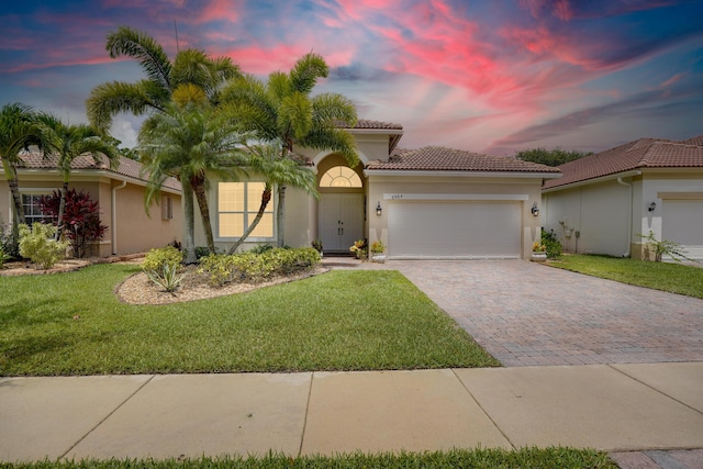 mediterranean / spanish house featuring a tiled roof, a front yard, stucco siding, decorative driveway, and a garage