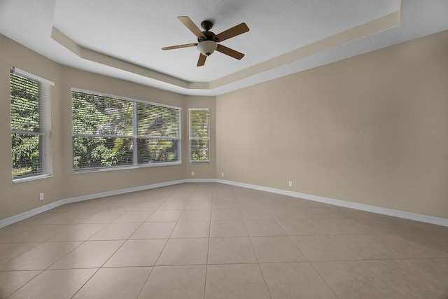 tiled empty room featuring a tray ceiling, baseboards, and ceiling fan