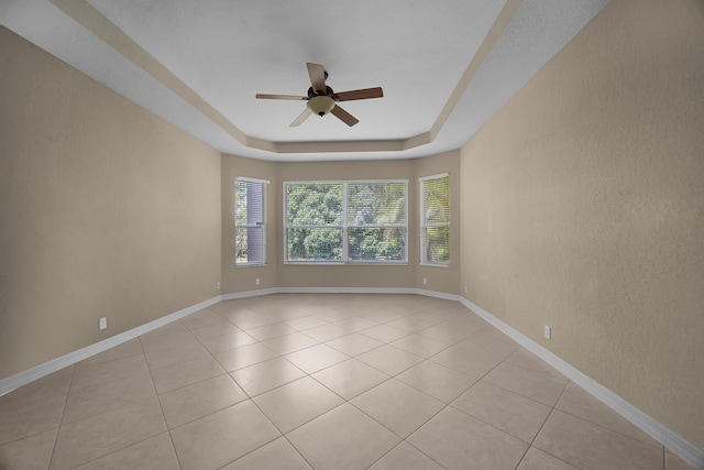 spare room featuring baseboards, a tray ceiling, light tile patterned floors, a textured wall, and a ceiling fan