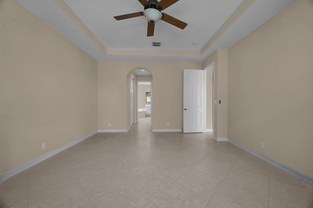 empty room featuring light tile patterned floors, a ceiling fan, baseboards, arched walkways, and a raised ceiling