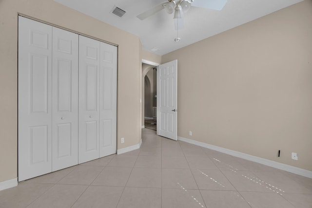 unfurnished bedroom featuring visible vents, baseboards, a closet, light tile patterned floors, and arched walkways