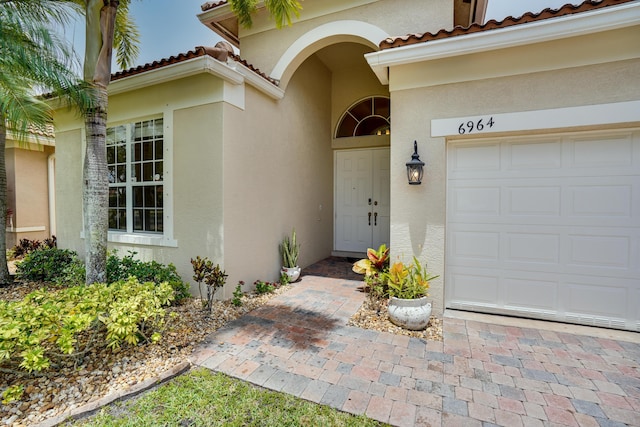 doorway to property featuring a tiled roof, a garage, and stucco siding