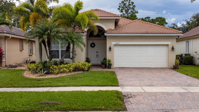 mediterranean / spanish house featuring stucco siding, decorative driveway, a front yard, an attached garage, and a tiled roof