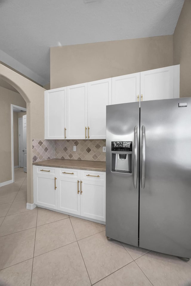 kitchen with white cabinetry, light tile patterned flooring, arched walkways, and stainless steel fridge