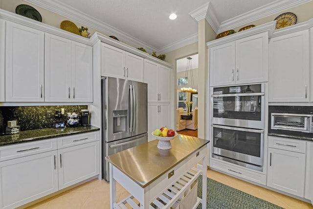 kitchen featuring stainless steel appliances, light tile patterned floors, tasteful backsplash, white cabinets, and ornamental molding