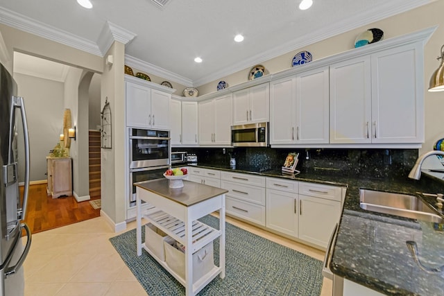 kitchen with appliances with stainless steel finishes, crown molding, sink, light tile patterned floors, and white cabinets