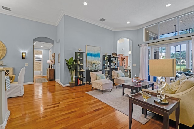 living room with crown molding, light hardwood / wood-style flooring, and a towering ceiling