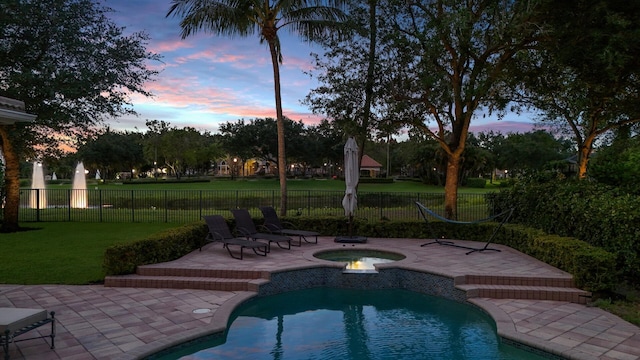 pool at dusk featuring an in ground hot tub, a patio area, and a lawn