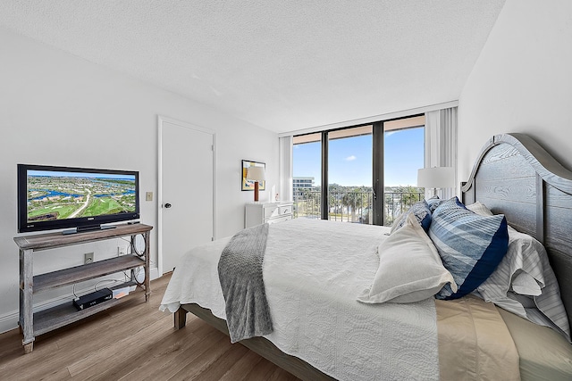 bedroom featuring floor to ceiling windows, a water view, a textured ceiling, and hardwood / wood-style flooring