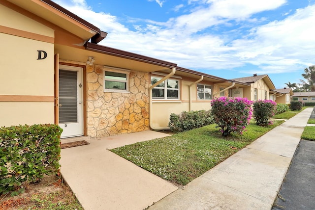 property entrance with stone siding, a lawn, and stucco siding