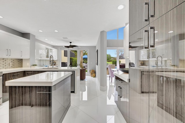 kitchen featuring ceiling fan, sink, a kitchen island, backsplash, and white cabinets