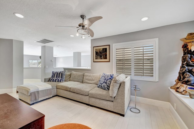 living room with ceiling fan, light wood-type flooring, and a textured ceiling