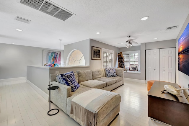 living room with a textured ceiling, light hardwood / wood-style flooring, and ceiling fan