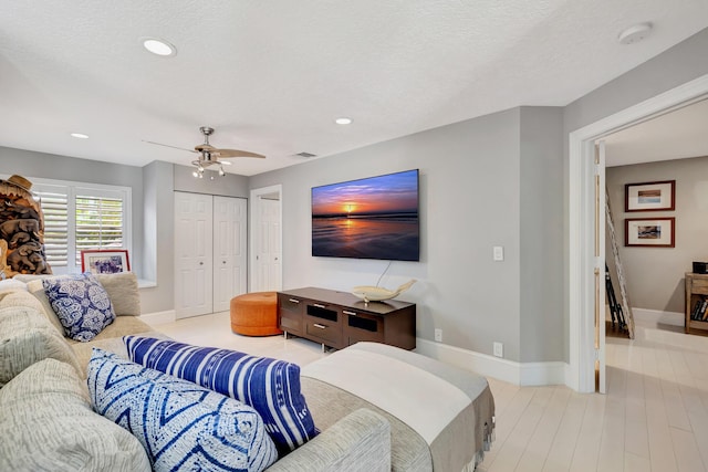 living room with ceiling fan, a textured ceiling, and light wood-type flooring