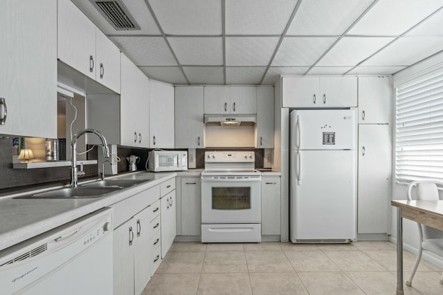 kitchen featuring a paneled ceiling, white appliances, sink, light tile patterned floors, and white cabinets