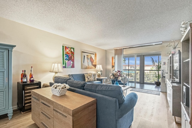 living room with wine cooler, floor to ceiling windows, a textured ceiling, and light wood-type flooring