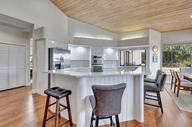 kitchen with appliances with stainless steel finishes, tasteful backsplash, wood ceiling, white cabinetry, and a breakfast bar area