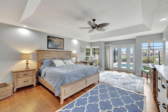 bedroom featuring a raised ceiling, multiple windows, ceiling fan, and access to outside