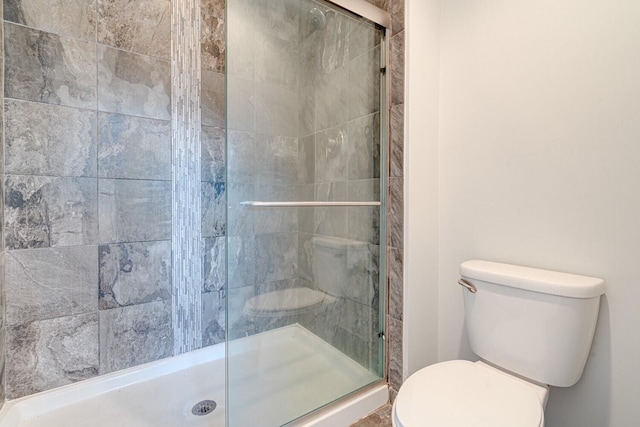 bathroom featuring a shower with door and toilet