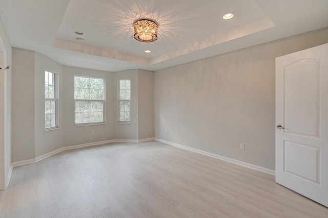 unfurnished room with light wood-type flooring and a raised ceiling