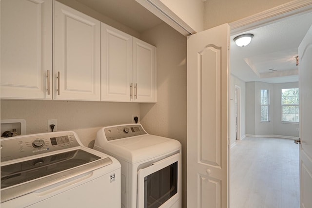 laundry room featuring washing machine and dryer, cabinets, and light wood-type flooring