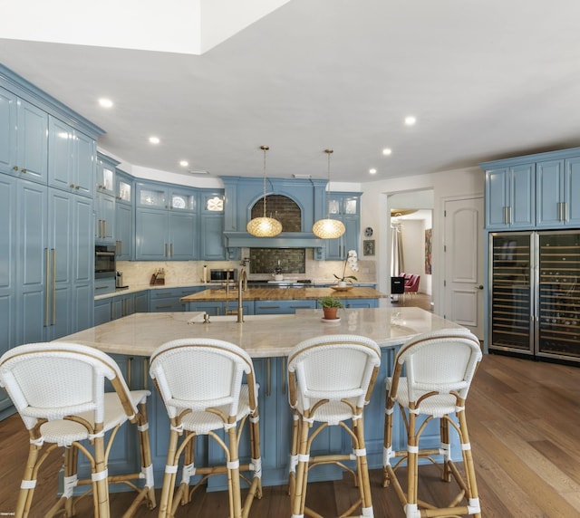 kitchen with decorative backsplash, hanging light fixtures, a center island with sink, and blue cabinets