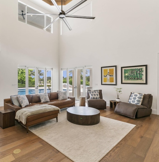 living room with ceiling fan, a high ceiling, wood-type flooring, and french doors