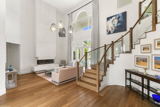 staircase with hardwood / wood-style flooring, a towering ceiling, and a fireplace