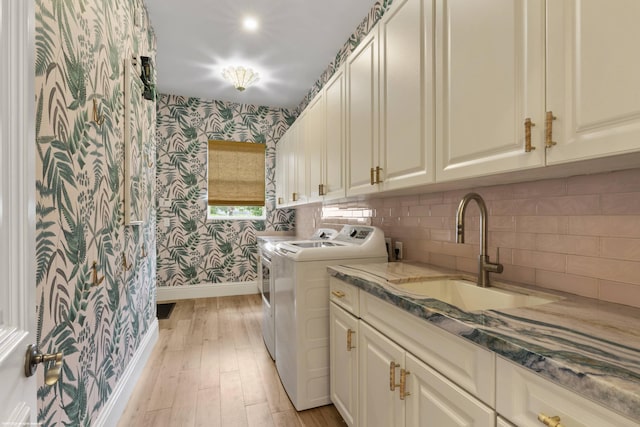 clothes washing area with cabinets, washer and dryer, light hardwood / wood-style floors, and sink