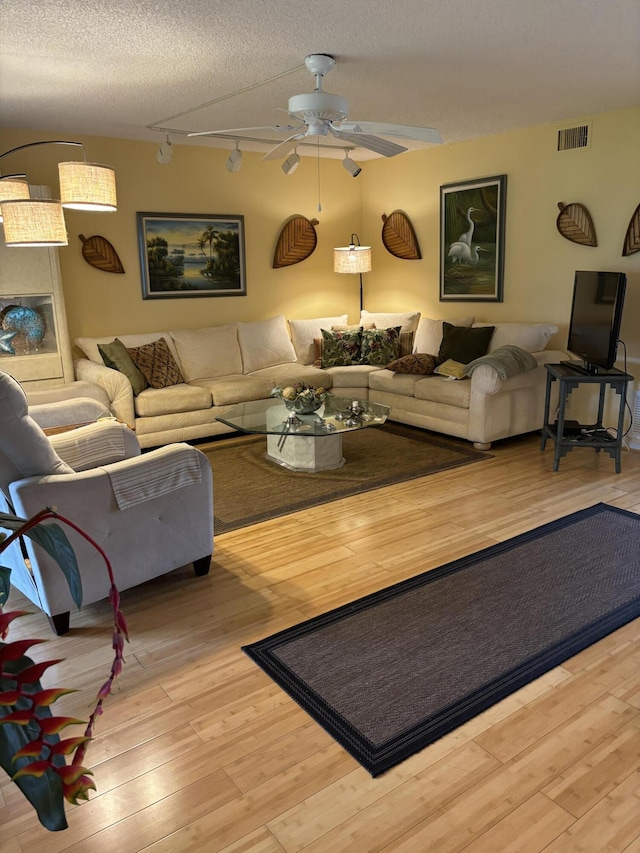 living room with a textured ceiling, ceiling fan, light wood-type flooring, and rail lighting