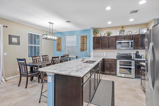 kitchen with appliances with stainless steel finishes, dark brown cabinetry, sink, a kitchen island, and hanging light fixtures