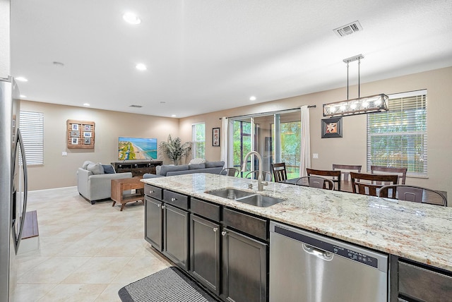 kitchen featuring light stone countertops, appliances with stainless steel finishes, dark brown cabinets, sink, and decorative light fixtures