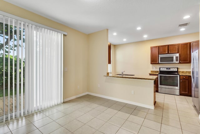 kitchen with light stone countertops, appliances with stainless steel finishes, kitchen peninsula, and sink