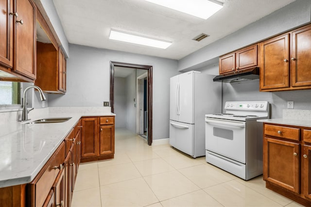 kitchen with light tile patterned flooring, light stone countertops, white appliances, and sink