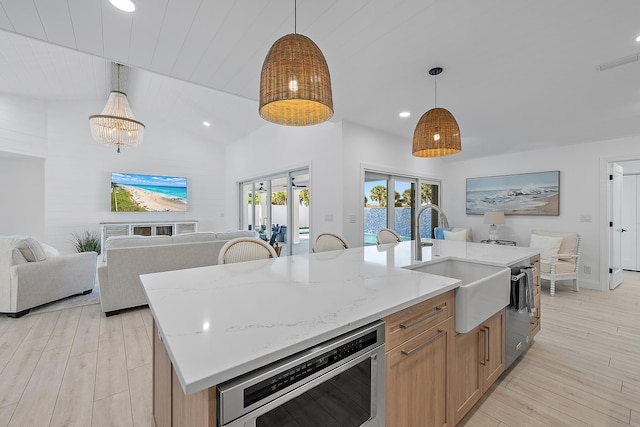 kitchen with pendant lighting, light stone counters, sink, and an island with sink