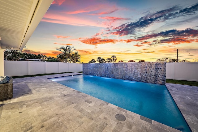 pool at dusk featuring pool water feature and a patio