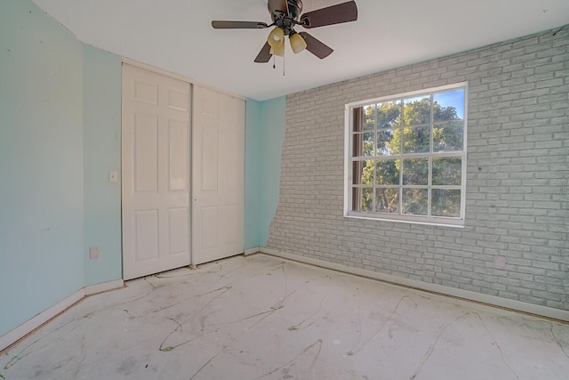 unfurnished bedroom with ceiling fan, brick wall, and a closet