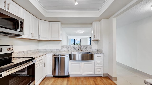 kitchen with a tray ceiling, sink, white cabinets, and appliances with stainless steel finishes