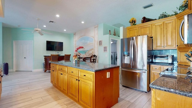 kitchen featuring appliances with stainless steel finishes, light hardwood / wood-style flooring, a kitchen island, and dark stone countertops