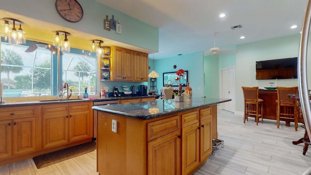 kitchen with a center island, dark stone counters, sink, light hardwood / wood-style flooring, and ceiling fan