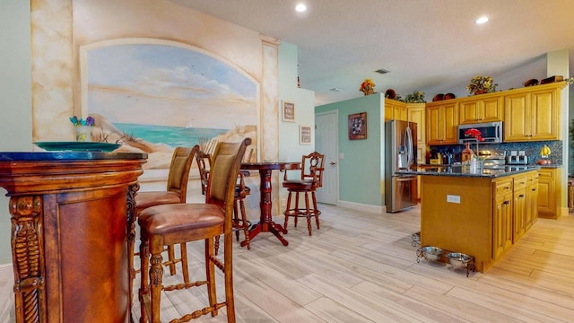 kitchen with stainless steel appliances, light hardwood / wood-style flooring, backsplash, dark stone counters, and a kitchen island