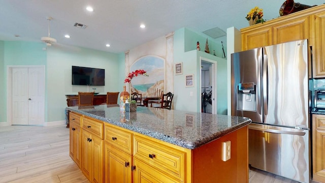 kitchen with a center island, stainless steel fridge, dark stone countertops, and light hardwood / wood-style floors