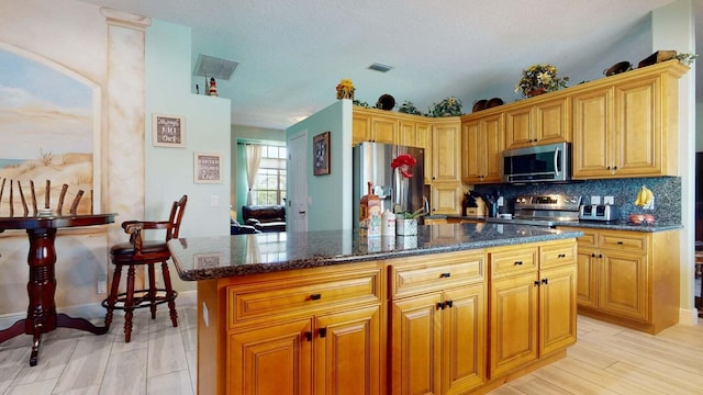 kitchen with a center island, stainless steel appliances, dark stone counters, decorative backsplash, and light wood-type flooring