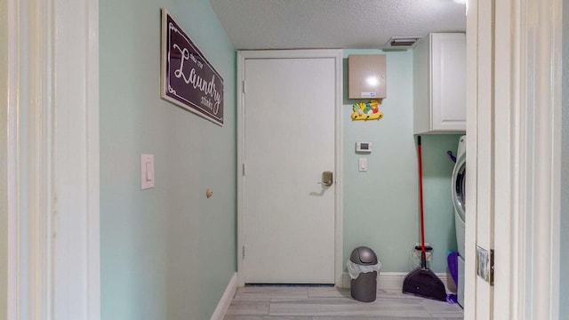 interior space with cabinets, a textured ceiling, and stacked washer and clothes dryer