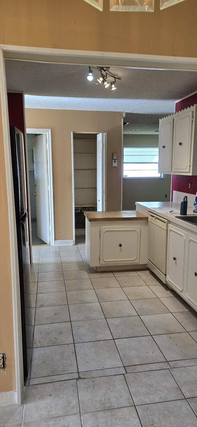 kitchen featuring kitchen peninsula, light tile patterned floors, dishwasher, white cabinetry, and fridge