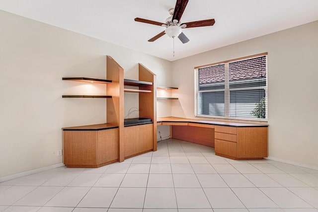 unfurnished office with ceiling fan, built in desk, and light tile patterned floors